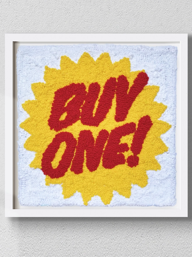 Buy One written in red writing in a yellow star on a white background in a white box frame mounted on a grey wall