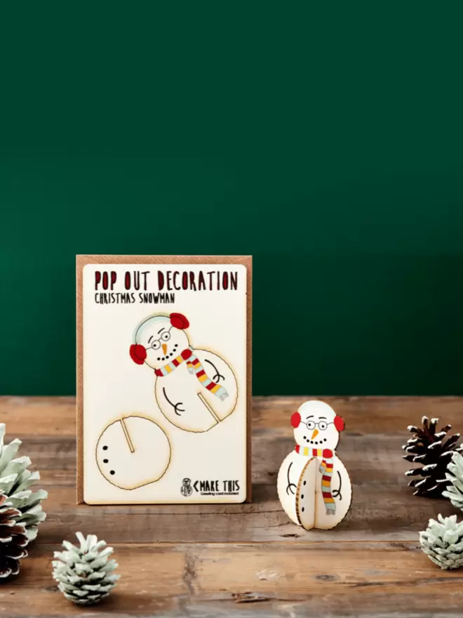 Pop out snowman Christmas decoration and Merry Christmas card and brown kraft envelope displayed on top of a wooden desk