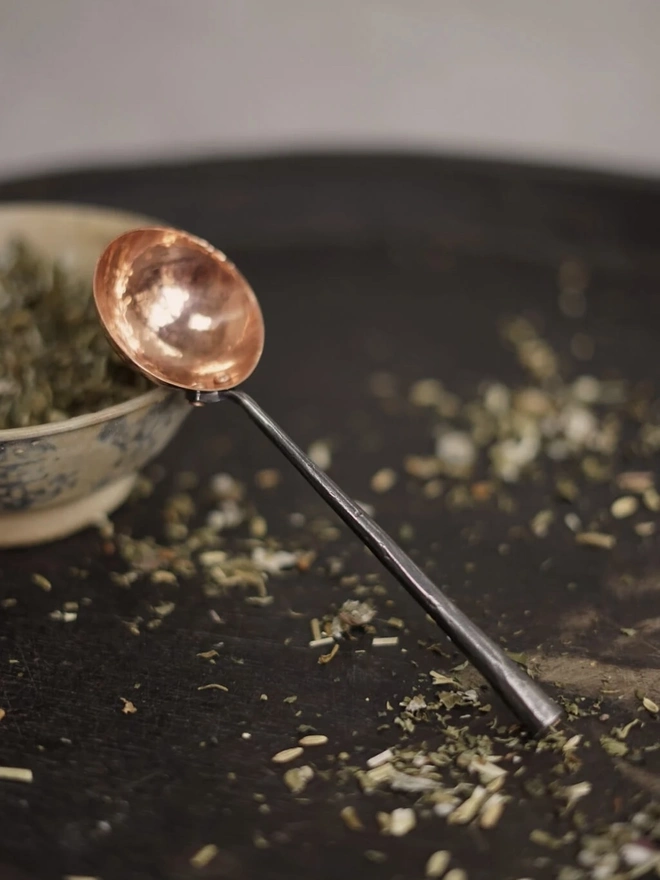 Copper And Stainless Steel Scoop, a metal scoop sitting on a bowl of herbs. 