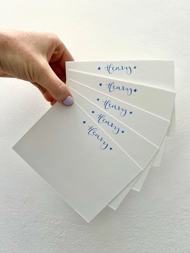 White notecards with Henry written in blue calligraphy at the top of each card, with one star either side of the name.