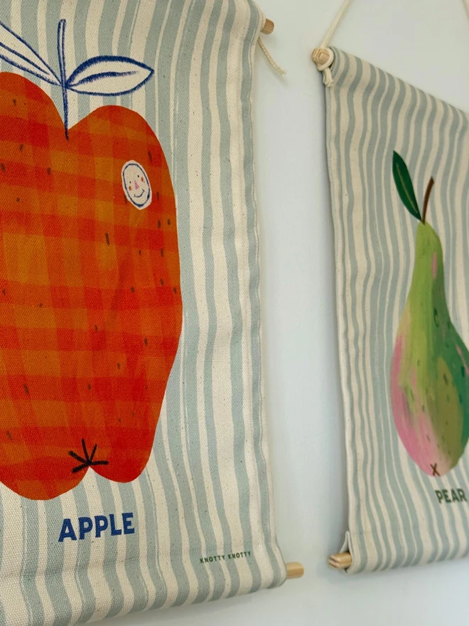 Cotton Lemon Wall Hanging, hanging on a white wall next to other fruit. 