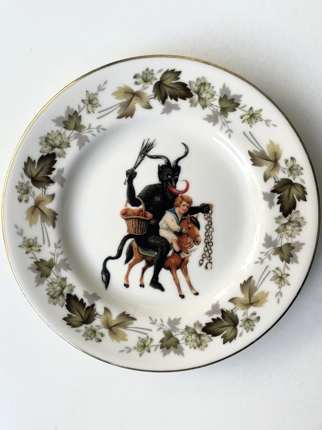 a naughty Christmas Krampus stealing a child, the image is victorian and is printed directly onto an ornate vintage plate