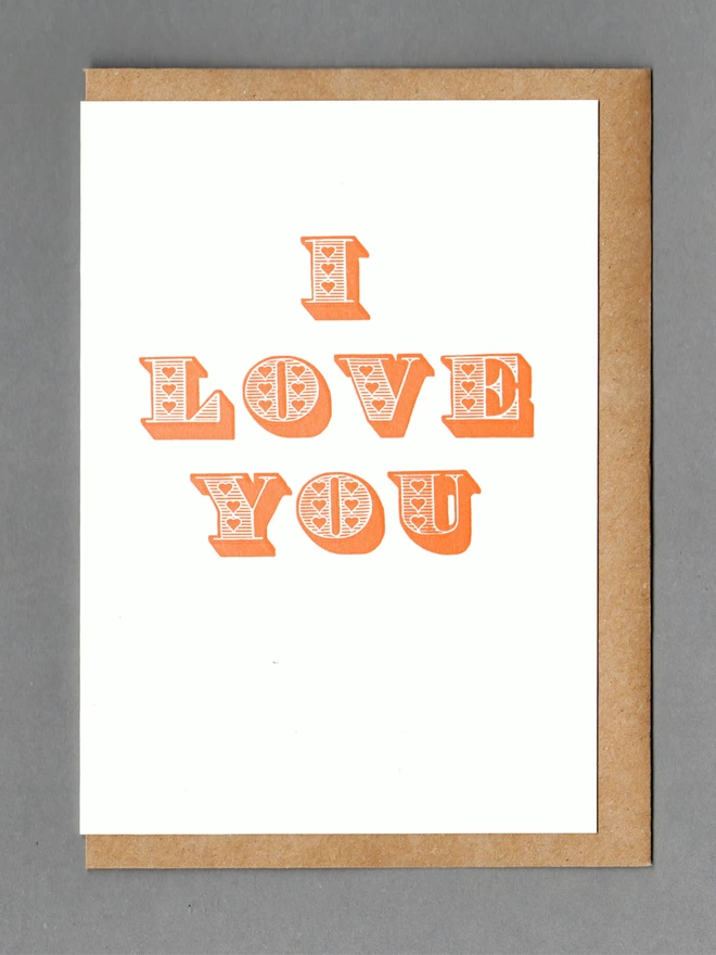 White card with orange text reading 'I LOVE YOU' with a kraft envelope behind it