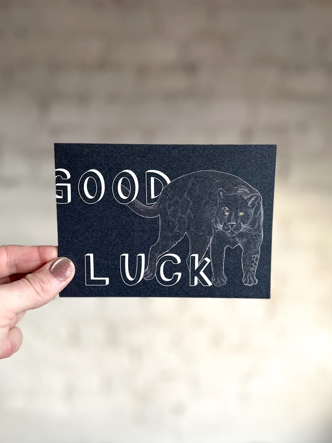 a dark grey greetings card featuring an illustration of a black panther with the text “good luck”