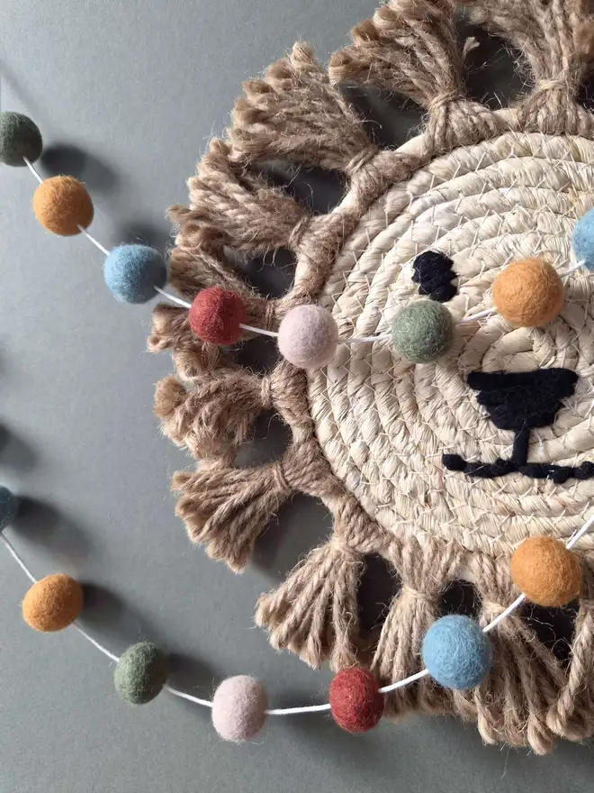 Felt ball garland hanging on a wall with a rattan lion in the background.