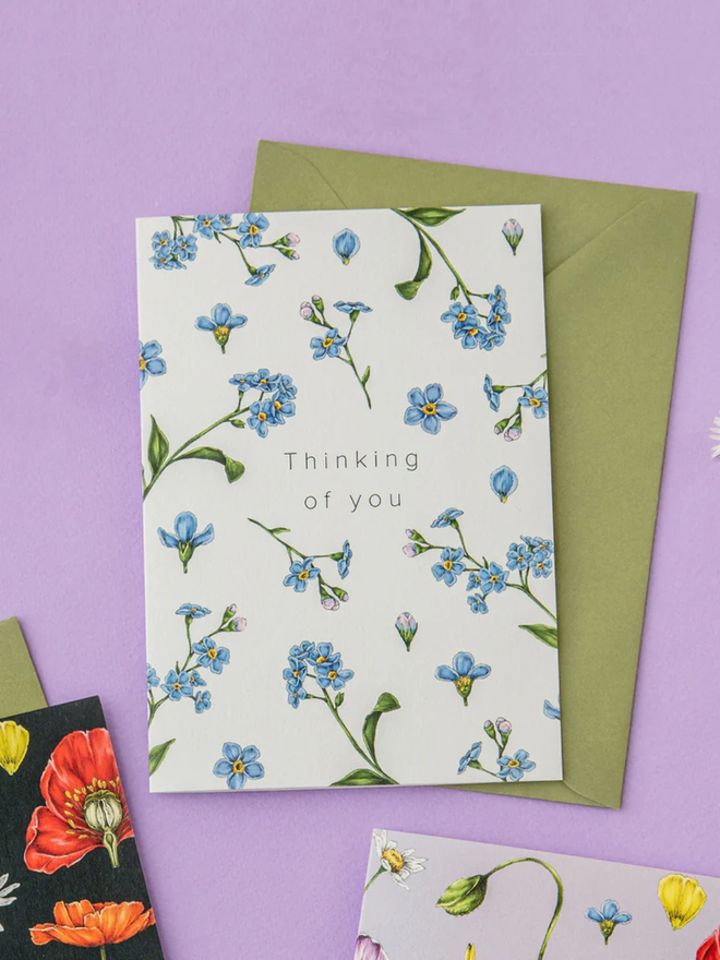 'thinking of you' illustrated champ de fleur card. a white floral card photographed against a purple background.