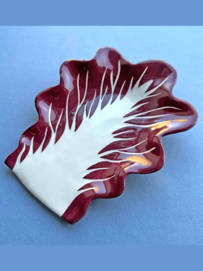 Radicchio Leaf Spoon Rest in Verona Red on a plain blue background
