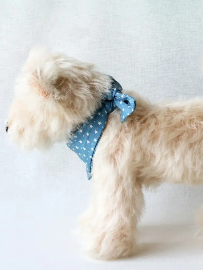 Handmade cream-colored teddy dog wearing a blue bandana standing against a plain background.