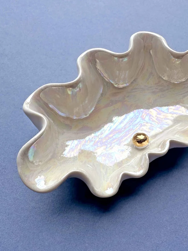 Porcelain clam shell pinch pot in shimmery white with gold mother of pearl in the middle of the shell, on a blue background