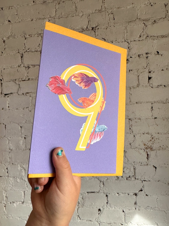 bright purple card with a big yellow number 9 and three bright illustrated betta fish with a bright yellow envelope