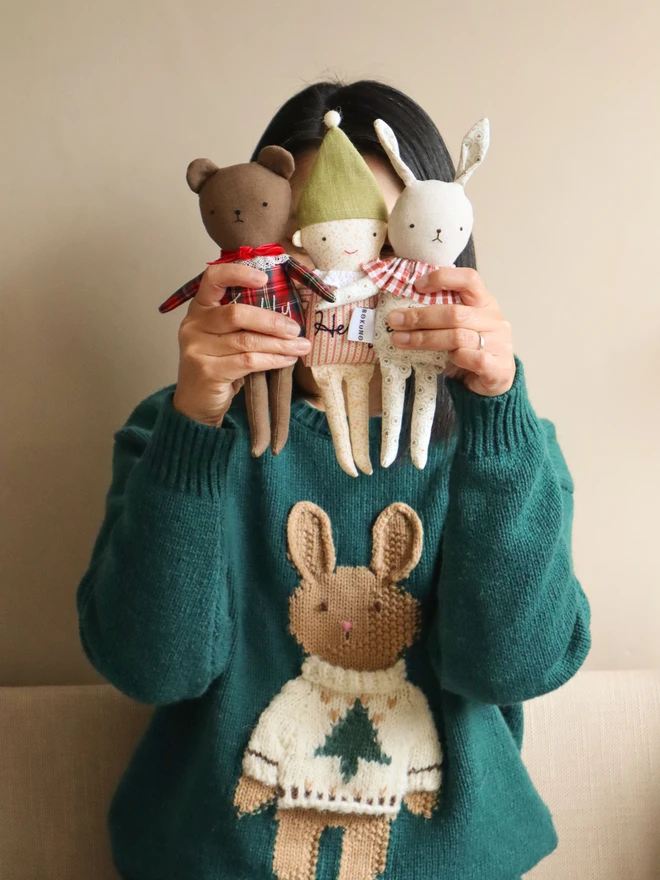 Handmade linen teddy bear wearing festive tartan outfits in green and navy with a green bow. It features delicate lace collars and embroidered faces. Held with Elf doll and bunny doll.