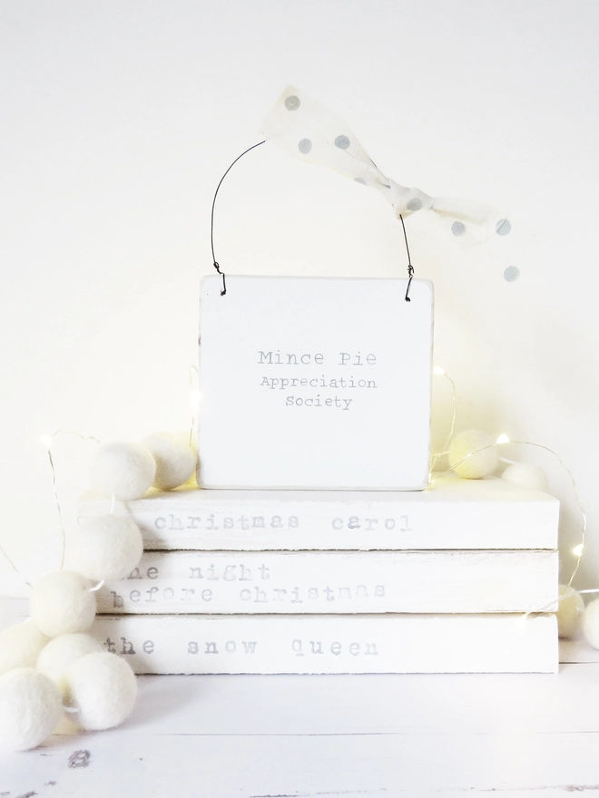 painted white sign with festive message strung with wire and decorated with ribbon.