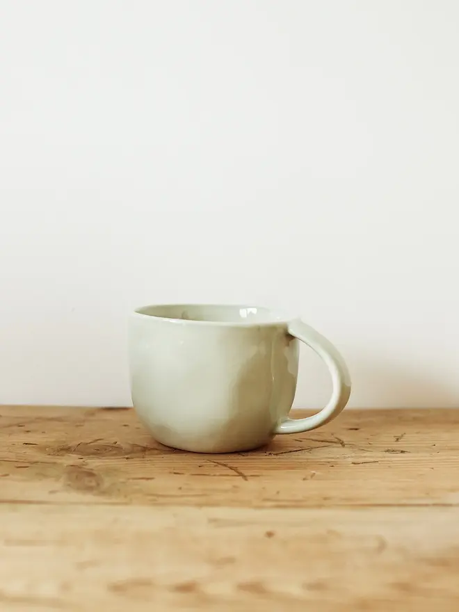 handcrafted stoneware mug. a green stoneware mug on a wooden bench.