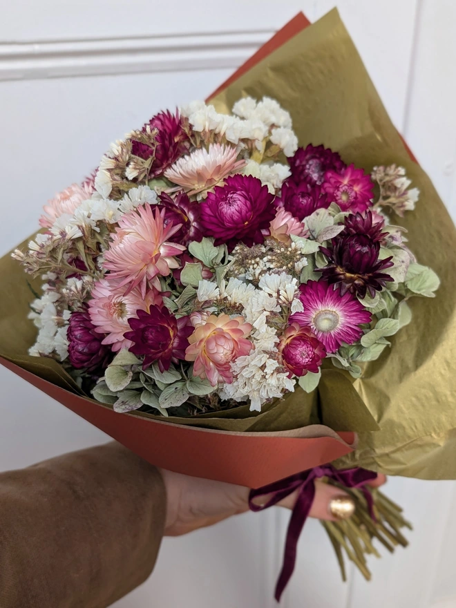 Lady holding a bunch of pink flowers wrapped in gold paper