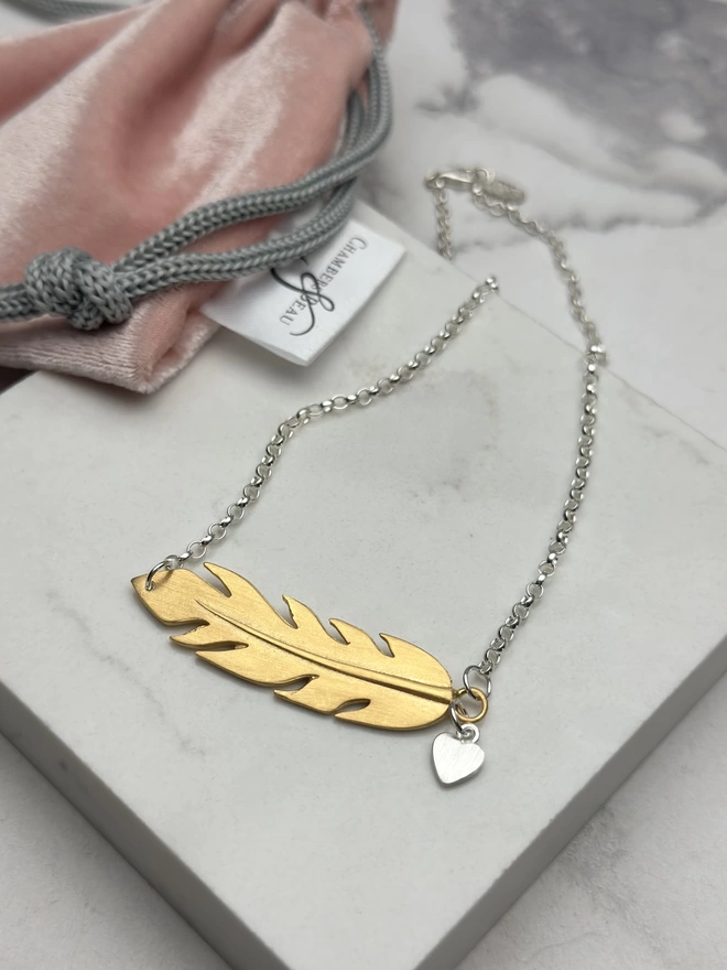 sterling silver chain with gold horizontal feather charm. a small silver heart charm hangs from the chain next to the feather