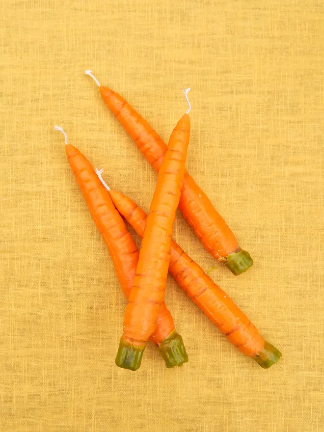 4 Fallow dinner carrot candles laid out on a mustard tablecloth 