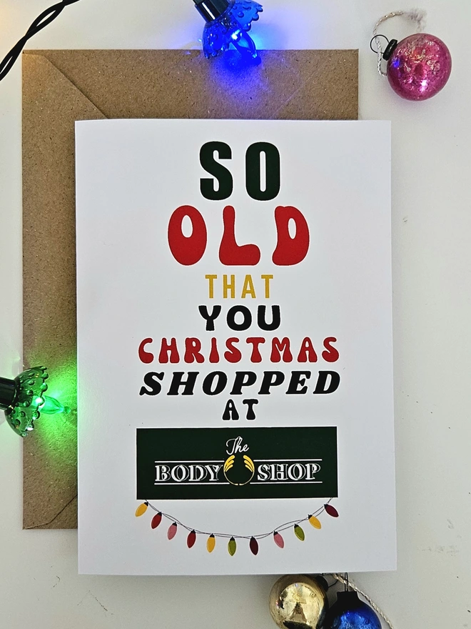 A photograph of the front of a humorous A6 greeting card illustrated using brightly coloured text and the retro shop logo. The text says so old  that you Christmas shopped at The Body Shop with string lights