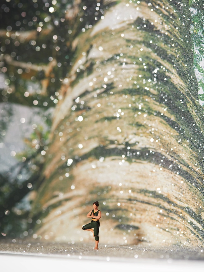 Miniature scene in an artbox showing a tiny figurine doing the yoga tree pose against an image of a magnificent sparkling tree