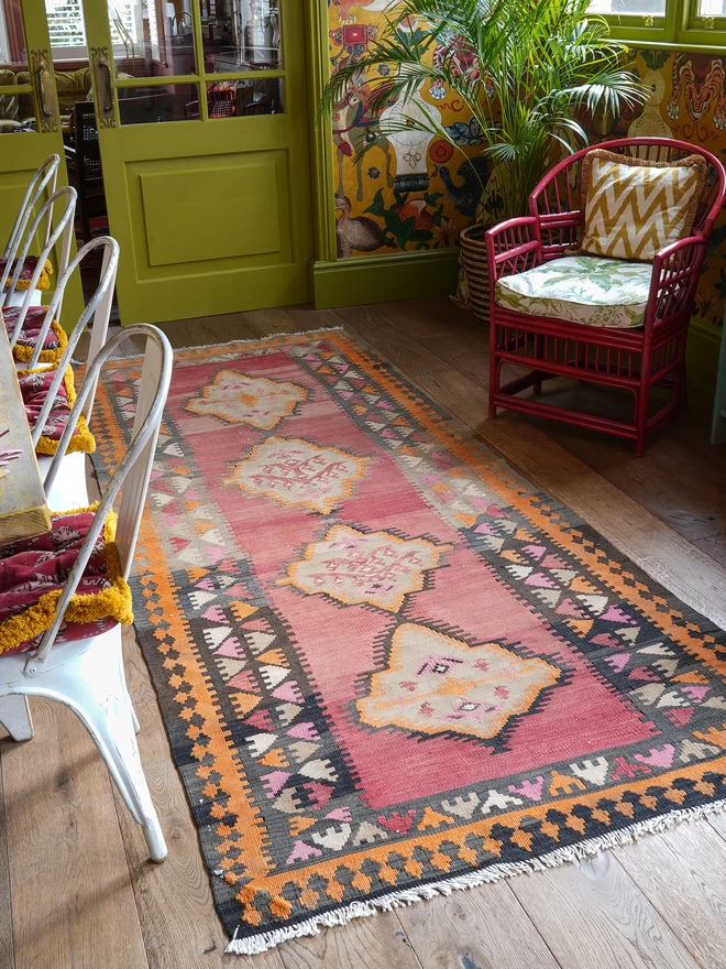 Orangey, red and black geometric vintage kilim hand woven rug on wooden floor in maximalist dining room with green woodwork