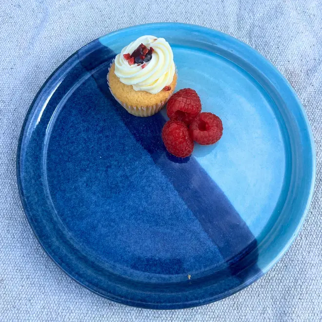 Landscape Side Plate, a colourful plate placed on a stone surface. It is accompanied by fruits and a sweet treat. 
