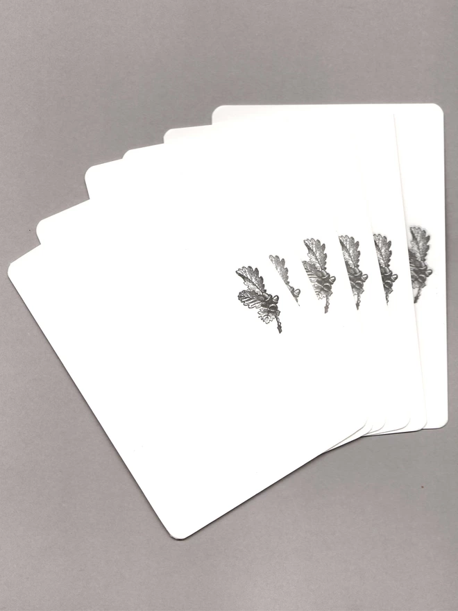 Six notecards with black acorns at the top laid out on a grey background