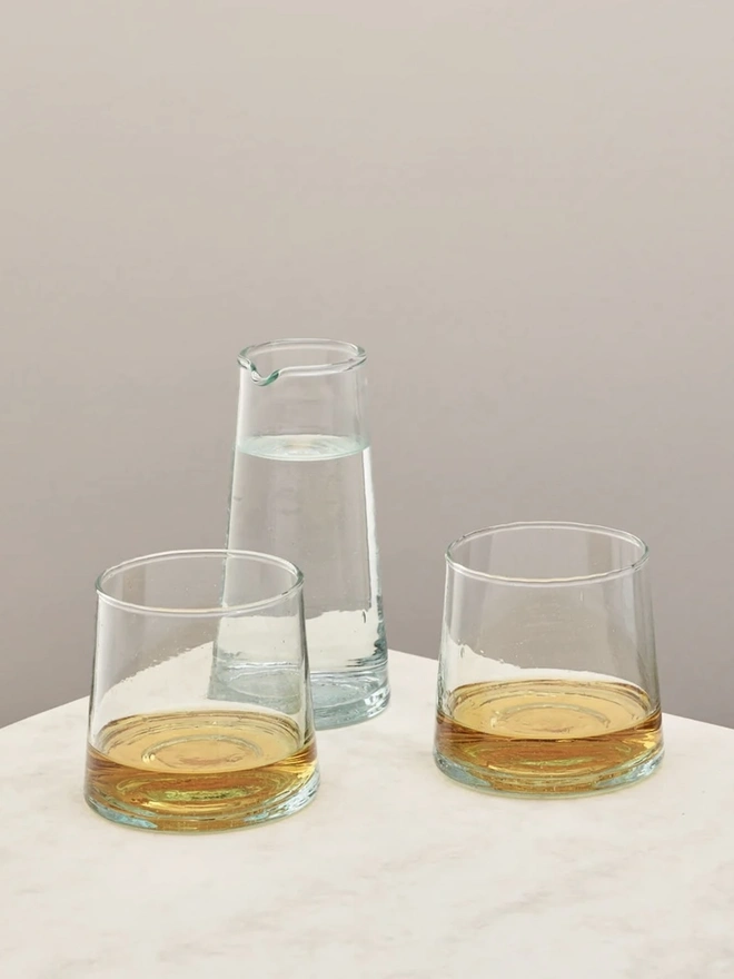 Whisky Glasses (Set Of 3), a set of whisky glasses and a jug sitting on a plain counter top against a grey backdrop. 