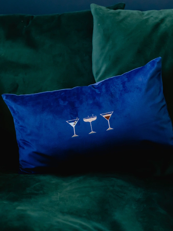 A navy blue velvet bolster cushion with cocktail embroidery