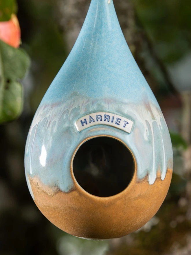 Personalised Blue Quartz Teardrop Bird Feeder hanging from a tree personalised with the name 'Harriet'
