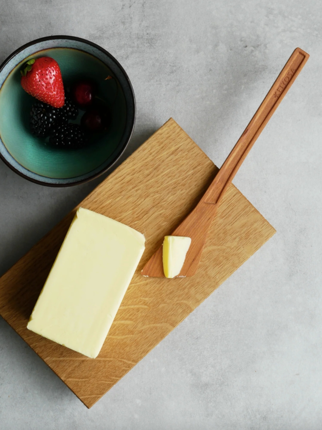 Wooden Butter Knife. A butter knife on a chopping board with butter, shown in use.