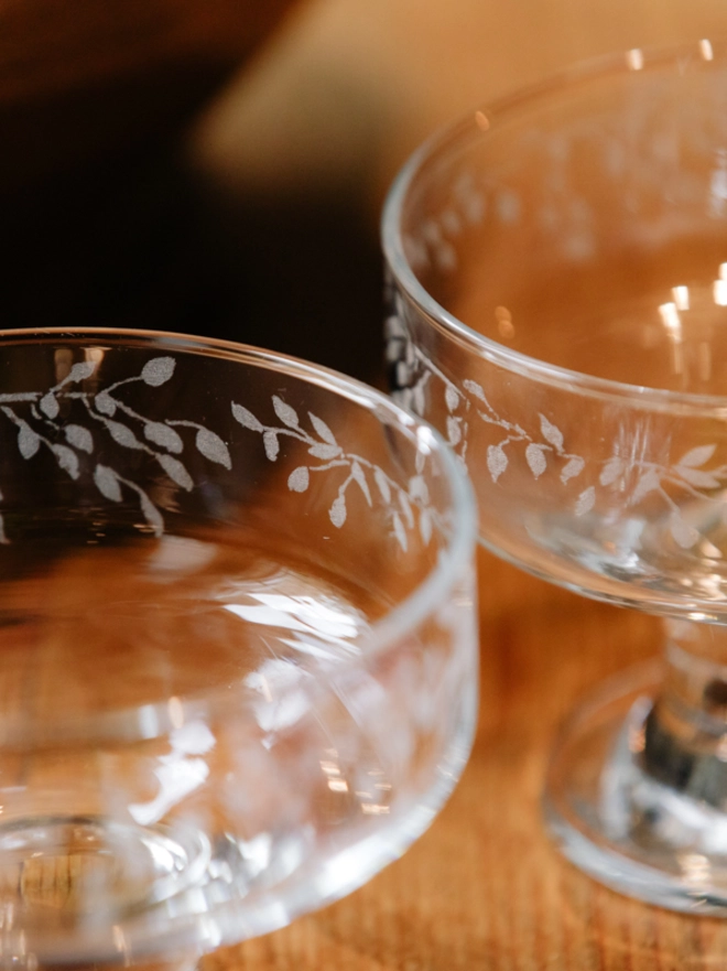 Two clear glass dessert bowls with an etched leaf pattern filled set on a rustic wooden table.