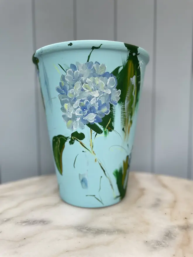 Hand painted terracotta floral plant pots pale blue background adorned in blue hydrangea flowers  