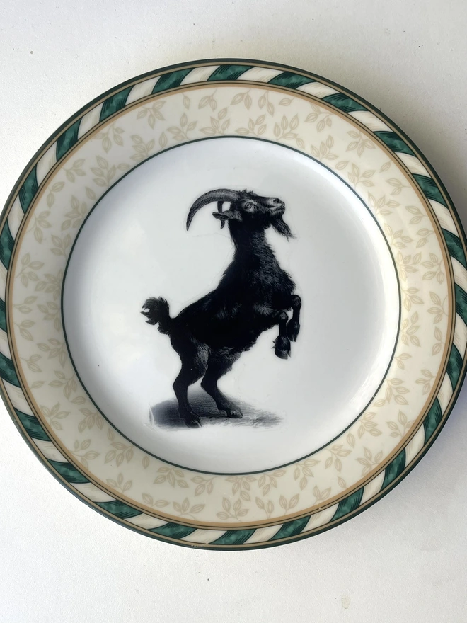 a vintage plate with an ornate border, in the centre of the plate is a vintage style black and white illustration of a Blac Phillip goat