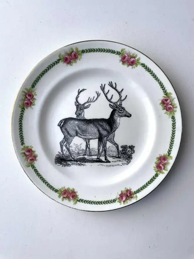 a vintage plate with an ornate border, an illustration of a pair of deer stags in the centre