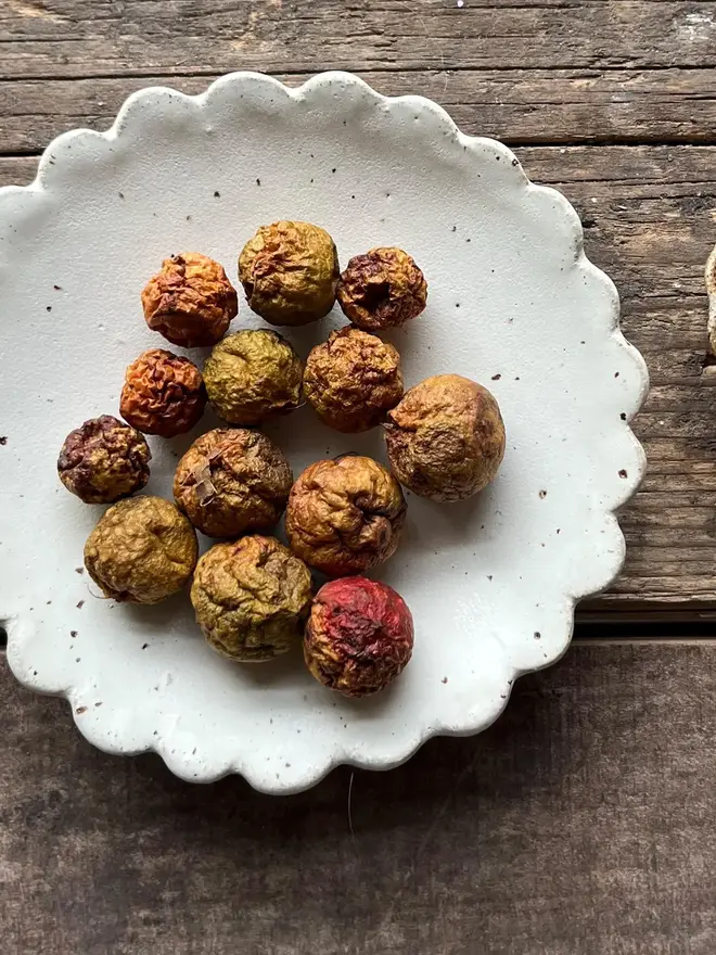 Handmade Scalloped Ceramic Dish, a ceramic dish on a wooden surface. It is accompanied by some lychees. 