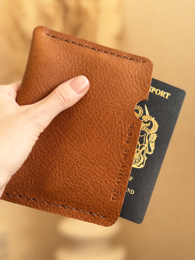 tan leather passport case with The Adventure begins hand stamped on it.
