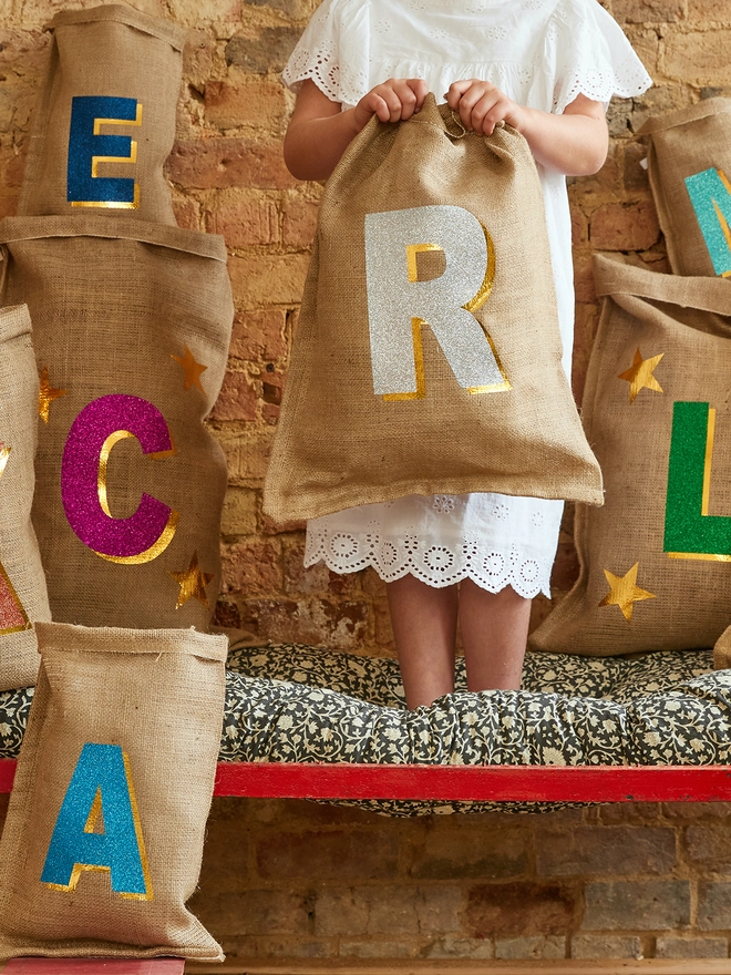 Personalised 3D initial Christmas sacks in various colours with small human holding a sack