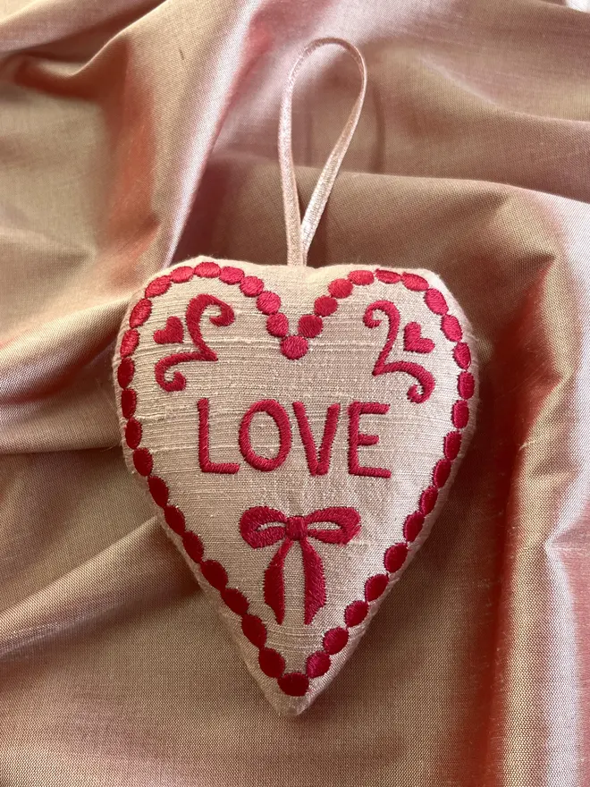 pink silk stuffed ornament with freehand embroidered design and "LOVE" in red thread with pink metallic ribbon