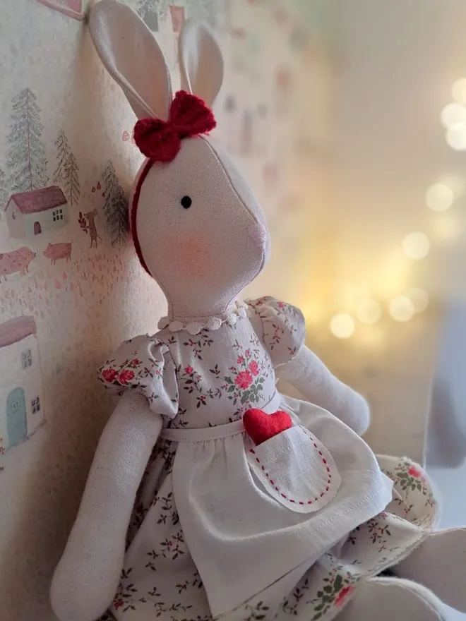 Side view of Veronica Bunny handmade from natural linen, wearing a vintage rose floral dress, linen apron and red felt heart detail