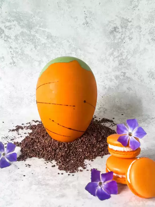 an orange carrot  easter egg with flowers and orange carrot cake filled macarons on a table