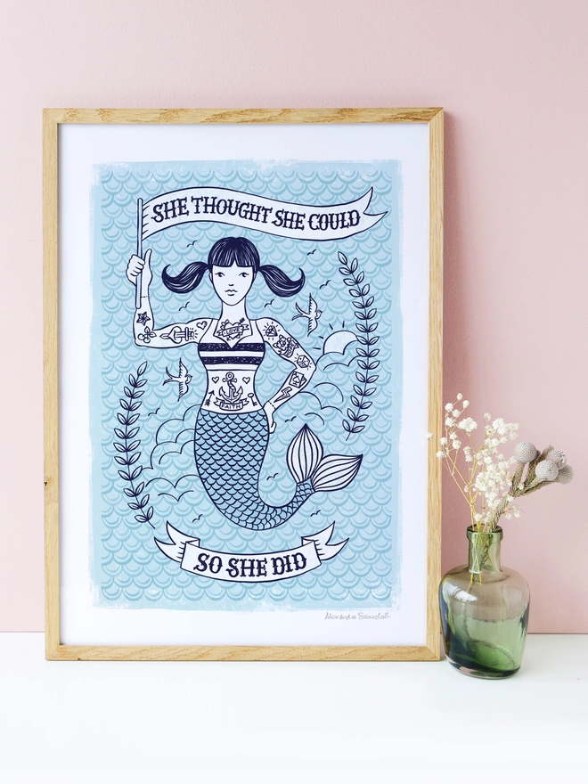 blue tattooed mermaid congratulations print with pink background and green vase with flowers