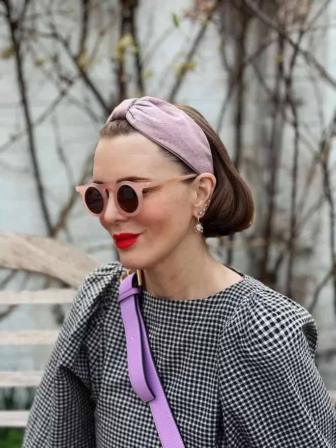 Vanessa Rose Ines Hairband in Lilac Pink seen on a woman wearing a purple cross-body bag and gingham.