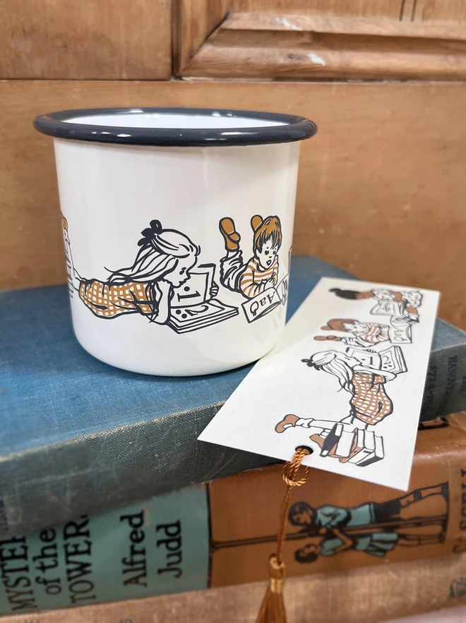 a large cream enamel mug with a grey rim featuring a screen printed illustration of children reading