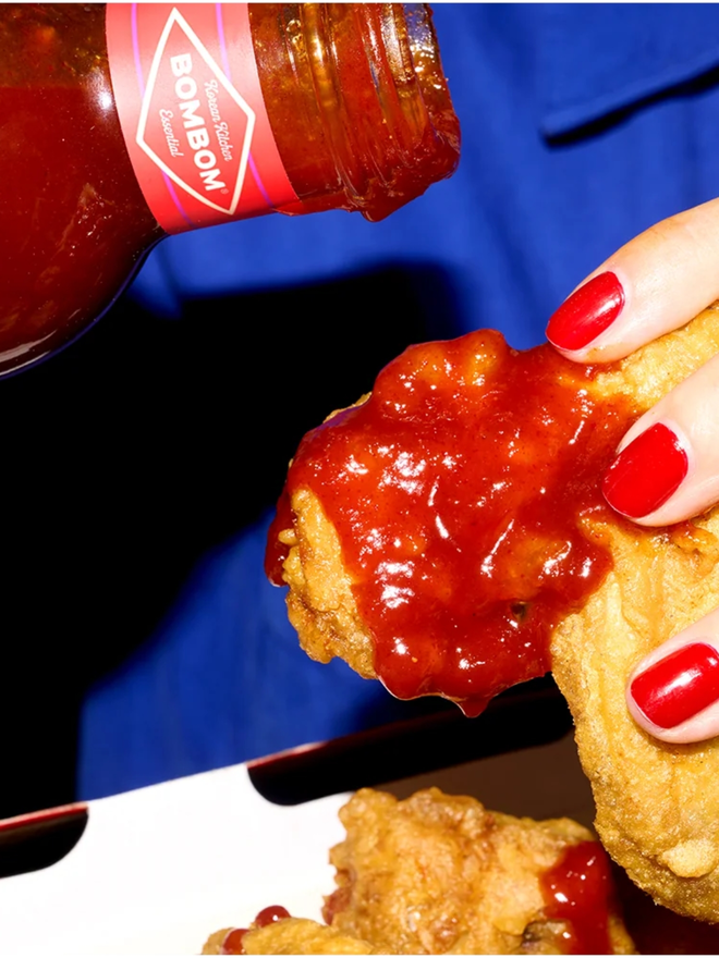 sweet and spicy korean bbq sauce. a close up of bbq sauce being poured on a piece of fried chicken.