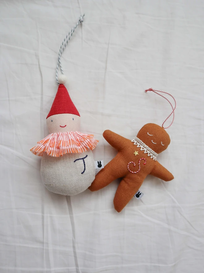 Brown linen gingerbread man christmas tree ornament with a letter hand embroidered in candy cane colours, star shaped sequin, crochet cotton lace around the neck, smile embroidered in white and candy cane colour string to hang. 