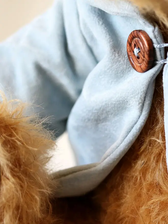 Handmade teddy bear with soft textured fur, wearing a blue jacket, posed against a plain background.