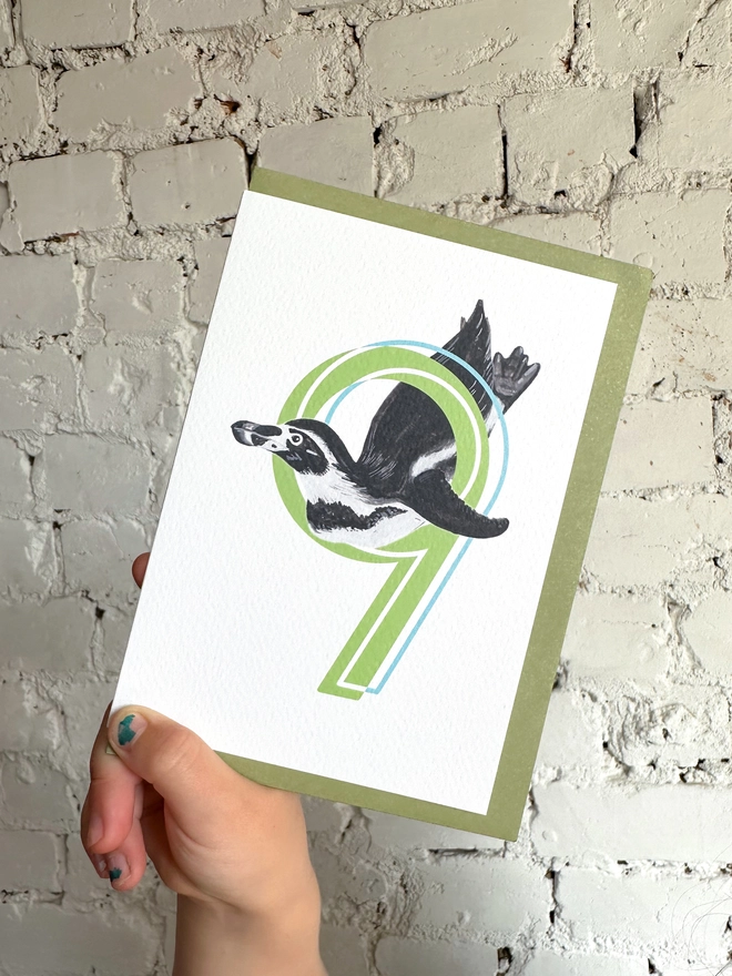 white card with a big green number 9 and a penguin illustration and a green envelope