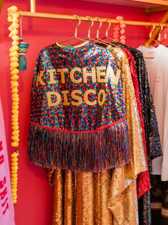 A multi-coloured maxi length cape with 'KITCHEN DISCO' across the back in gold text. The tinsel is rainbow,