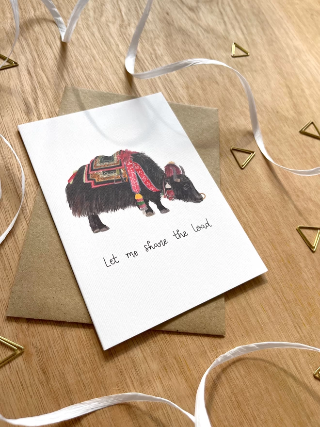 a greetings card featuring a domestic yak carrying a bag and the phrase “Let me share the load”
