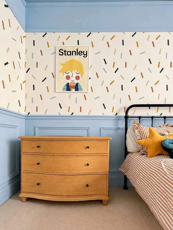 Children's room with a wooden dresser, bed, and colourful personalised wall art.
