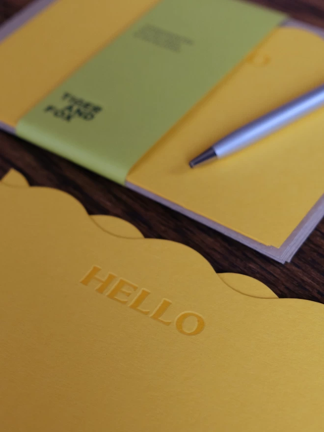 Wavy 'Hello' notecard set with green paper bellyband and pen.